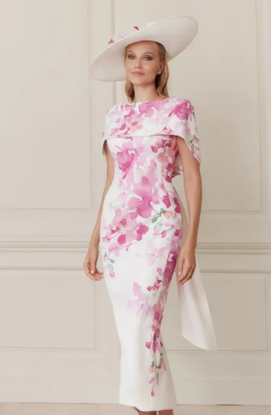Elegant woman in a white dress with pink floral design and matching wide-brimmed hat. The setting is sophisticated, evoking a sense of grace.